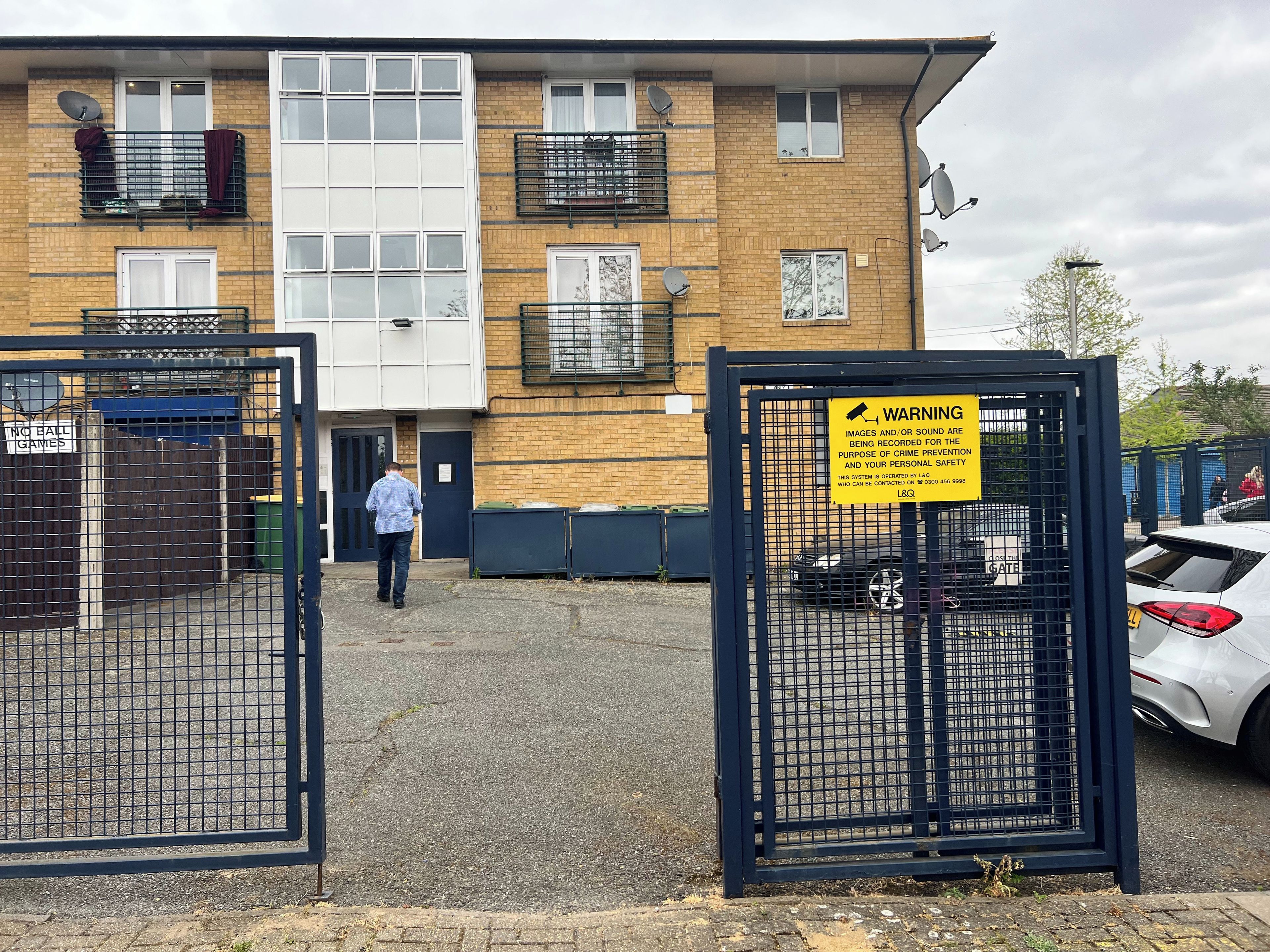 A gated entrance to a building with multiple windows and balconies, a sign warning of surveillance, and a parked car.