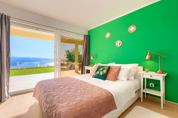 Un dormitorio con pared verde, una cama grande, una mesita de noche y vistas al exterior.