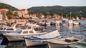 A marina with several boats docked, surrounded by buildings and a hilly backdrop.