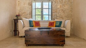 A stone-walled room with a white sofa, colorful cushions, and a wooden chest of drawers.