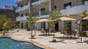 A pool area with lounge chairs and umbrellas, surrounded by a building with multiple floors and balconies.