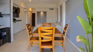 A dining area with a wooden table and chairs, a television mounted on the wall, and a plant in the corner.