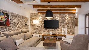 A living room with a stone wall, a flat-screen TV, a wooden coffee table, and a sofa. - Villa Klementina - Three Bedroom Villa, Sleeps 6 (Bicine)