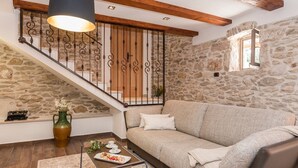 Un salon chaleureux avec un mur en pierre, un escalier en bois, un canapé et une petite table sur laquelle sont disposés des en-cas.