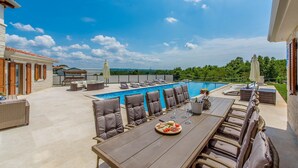 Un espace aménagé au bord de la piscine, comprenant une table à manger, des chaises longues et offrant une vue sur la piscine et la végétation environnante.