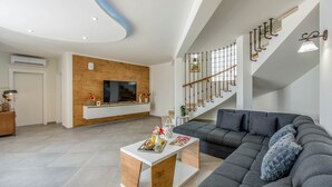 Un salon moderne avec un canapé d’angle gris, une table basse blanche sur laquelle se trouve un plateau de collations, un mur d’accent en bois et un escalier agrémenté de rampes décoratives.