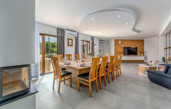A modern dining area with a round table, wooden chairs, and a TV in the background.