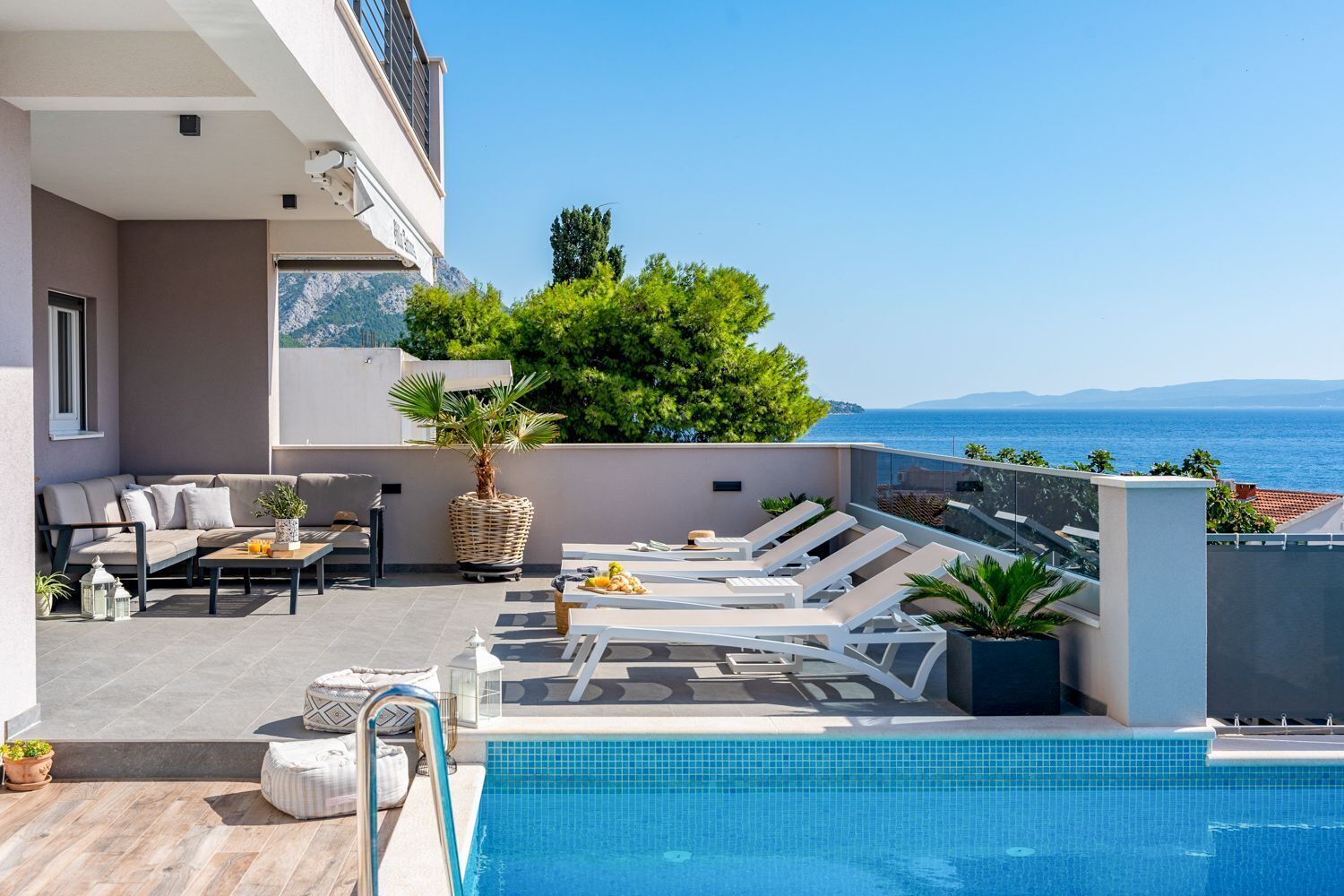 Ein Poolbereich auf dem Dach mit Liegestühlen, einer Sitzecke und Blick aufs Meer.