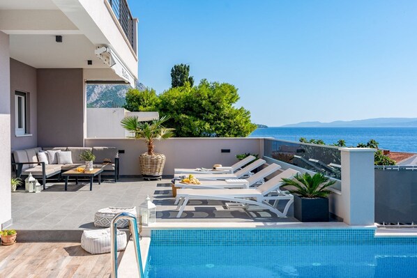 A rooftop pool area with lounge chairs, a seating area, and a view of the sea.