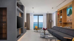 Una sala de estar moderna con un sofá gris, sillones amarillos, un televisor de pantalla plana y un amplio ventanal con vistas al mar.