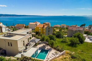 A residential area with a pool, houses with red roofs, and a view of the sea.