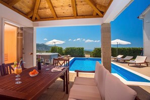 Un espace aménagé au bord de la piscine, avec une table en bois, des chaises longues et une vue sur un paysage montagneux.