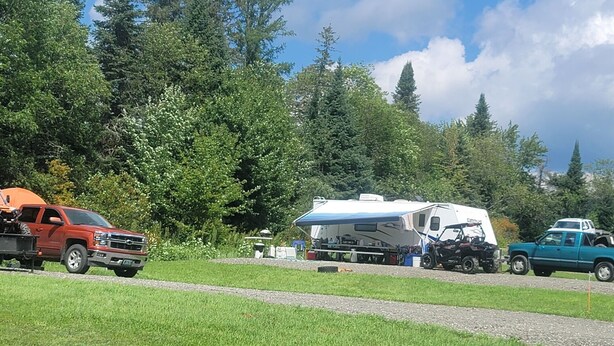 A campsite with a trailer, a red truck, and a green truck. - 09) The RV Campsite 5 (Stewartstown)