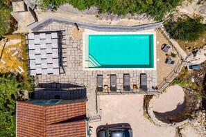 Vista aérea de una propiedad con piscina, sillones de descanso y un muro de piedra.