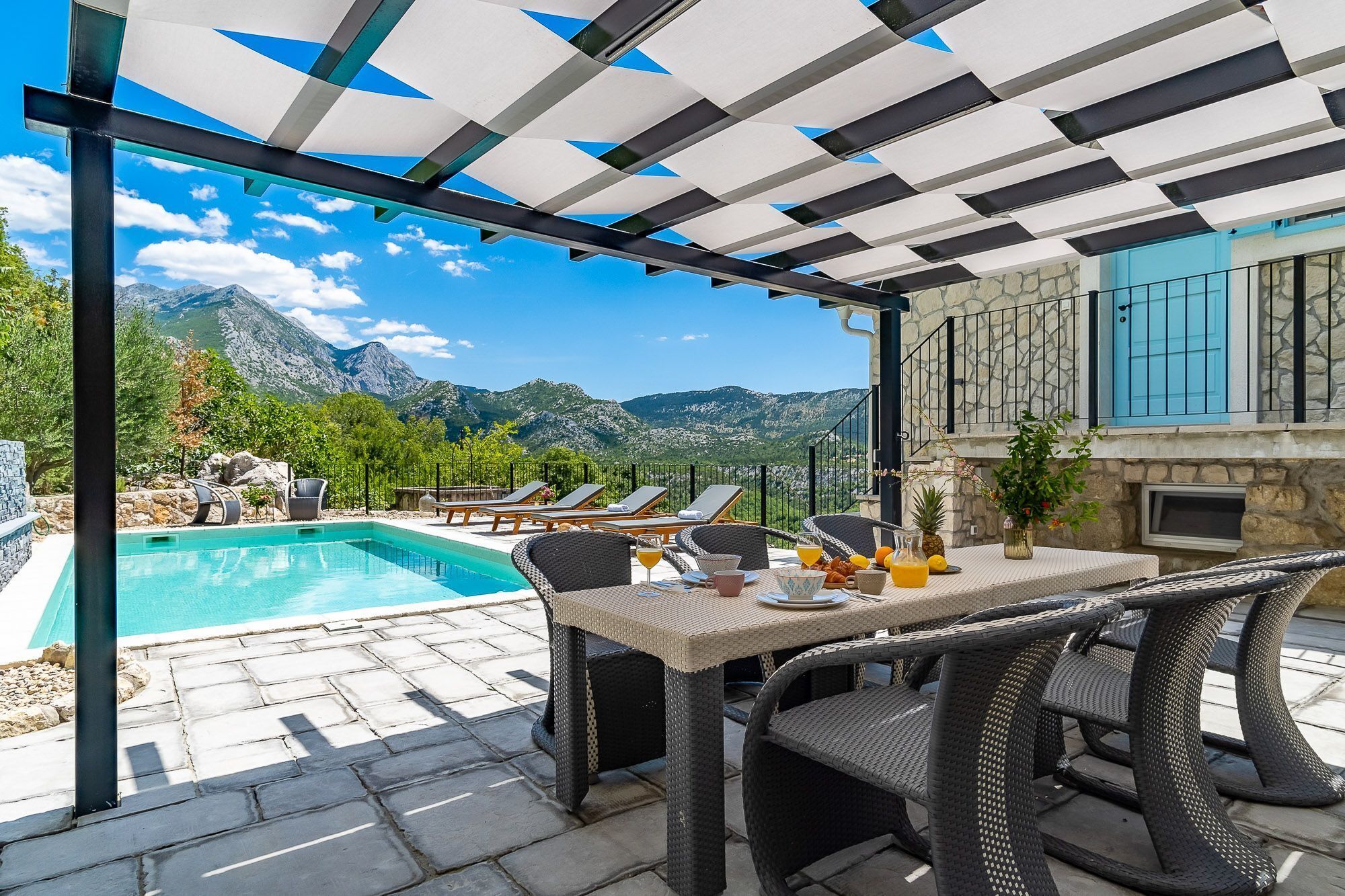 A poolside area with a view of mountains, outdoor seating, and a table with drinks.