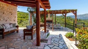 A stone patio with wooden furniture, a pergola with vines, and a view of hills. - Villa Fioretta - Four Bedroom Villa, Sleeps 8 (Ionian Islands)