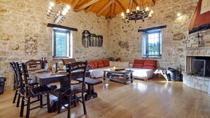 A rustic stone-walled room with a wooden ceiling, a dining table set with chairs, a sofa, and a fireplace. - Villa Fioretta - Four Bedroom Villa, Sleeps 8 (Ionian Islands)