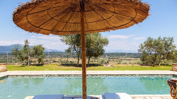 A poolside area with a thatched umbrella, lounge chairs, and a view of a landscape with trees and mountains. - Villa Fioretta - Four Bedroom Villa, Sleeps 8 (Ionian Islands)
