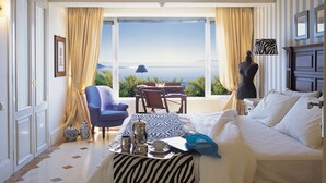 A hotel room with a bed, a chair, a table, and a view of the sea.