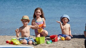 Three children playing with sand toys on a beach.
