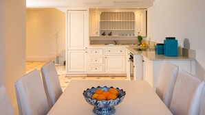 A modern kitchen with white cabinetry, a dining table with a bowl of fruit, and a staircase leading to another level.