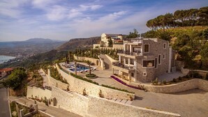 A modern stone building with a pool, surrounded by a stone wall and trees, overlooking a valley.