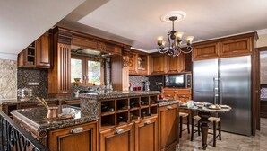 A spacious kitchen with wooden cabinets, granite countertops, a stainless steel refrigerator, and a bar area.