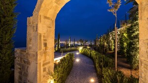 A stone archway leading to a pathway with a view of a cityscape at night.