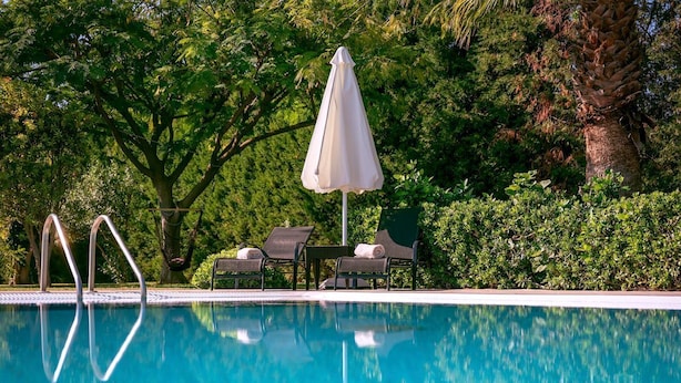 A swimming pool with lounge chairs and an umbrella, surrounded by lush greenery. - Villa Kalvos - Five Bedroom Villa, Sleeps 10 (Kolympia)
