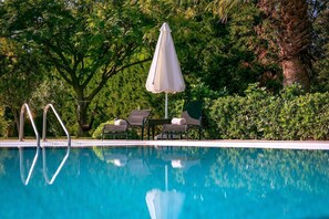 Ein Swimmingpool mit Liegestühlen und einem Sonnenschirm, umgeben von üppiger Vegetation.