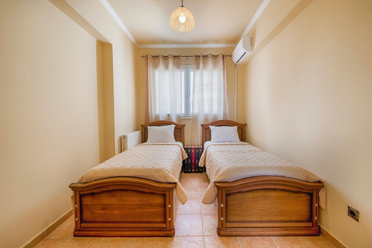 A room with two wooden beds, a window with curtains, and a ceiling light.