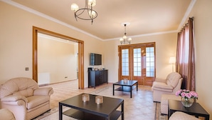 A spacious living room with beige sofas, a dark coffee table, and a chandelier. - Villa Kalvos - Five Bedroom Villa, Sleeps 10 (Kolympia)