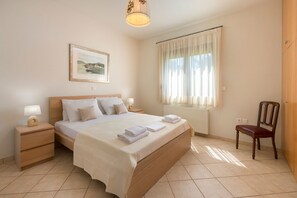 A neatly arranged bedroom with a bed, bedside tables, a chair, a window with curtains, and a wall-mounted picture.
