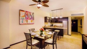 A dining area with a table set for four, a ceiling fan, and a kitchen in the background.