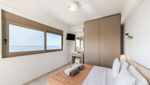 Une chambre d’hôtel moderne dotée d’un grand lit, d’une armoire, d’une télévision et offrant une vue sur la mer.