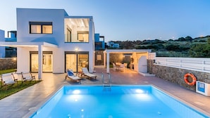 Une maison moderne à deux étages, dotée d’une piscine, d’un espace extérieur aménagé et d’un mur en pierre.