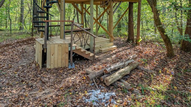 Une cabane dotée d’une terrasse en bois et d’un escalier en colimaçon, entourée d’une forêt.