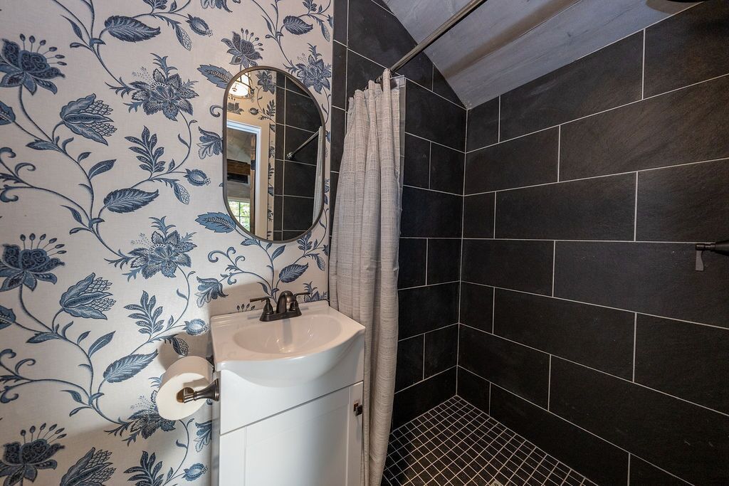 Un baño con lavamanos blanco, un espejo y una zona de ducha con azulejos oscuros.