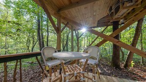 Une terrasse en bois avec une table et des chaises, entourée d’arbres.