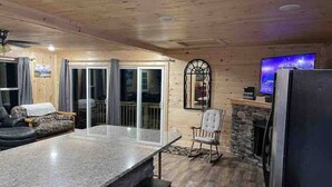 A cozy cabin interior with a stone fireplace, a large dining table, a television, and a sliding glass door leading to a balcony. - Crestview-Spectacular 3 bed 3 bath 5 min to slopes (Banner Elk)