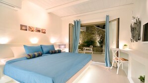 Een slaapkamer met een groot bed, nachtkastje, stoel en uitzicht op een stenen muur en buitenruimte.
