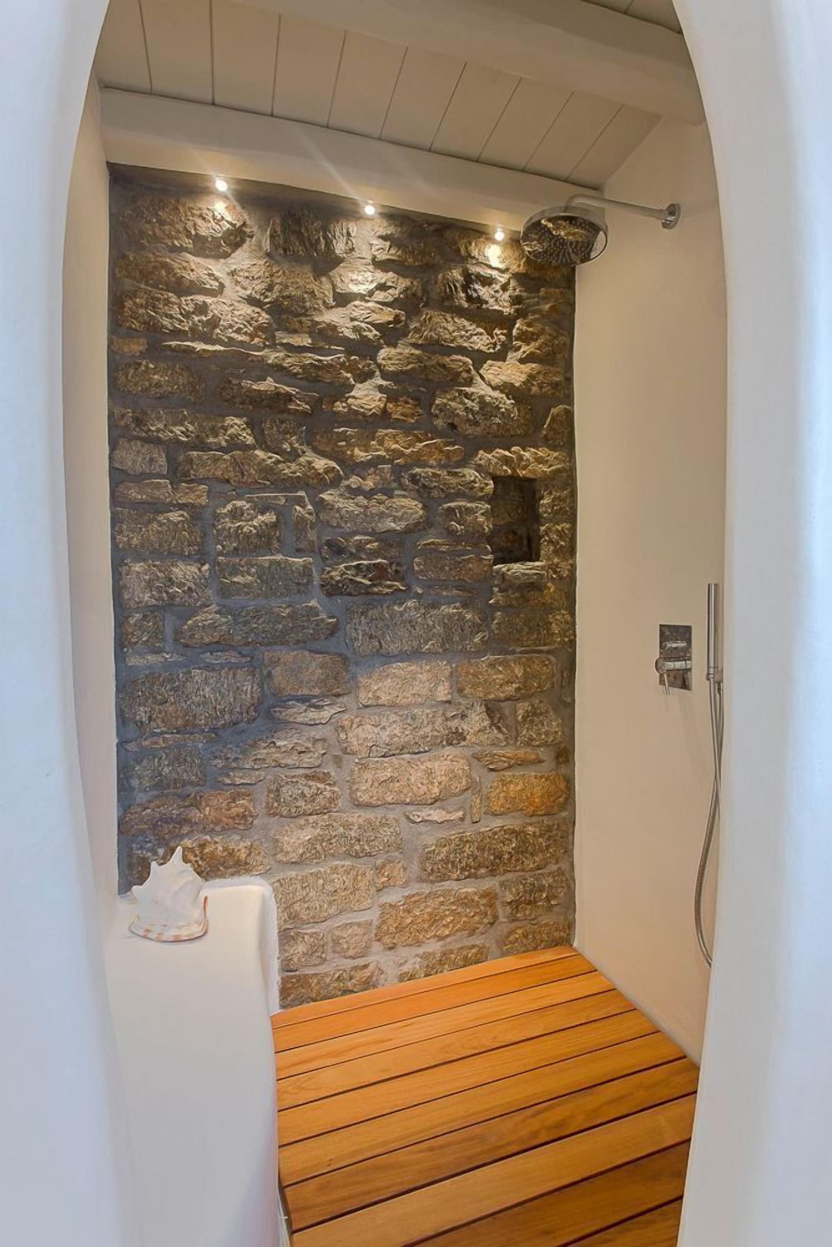 Una ducha con pared de piedra y suelo de madera.