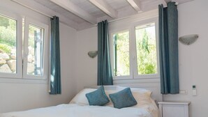Ein Schlafzimmer mit einem Bett, zwei Kissen, einem Nachttisch, einer Wanduhr und Vorhängen an den Fenstern.
