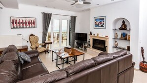 Ein Wohnzimmer mit braunem Ledersofa, Fernseher, Kamin und einem Balkon mit Vorhängen.
