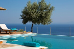 Piscina con vista despejada al mar, una silla de descanso y un árbol.