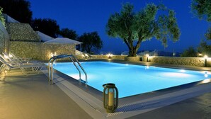 A swimming pool with lounge chairs and a stone wall. - Villa Ipsos - Five Bedroom Villa, Sleeps 9 (Spartilas)