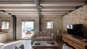 A spacious living room with a stone wall, a large TV, and a sofa. - Villa Kothreas - Four Bedroom Villa, Sleeps 8 (Kothreas)