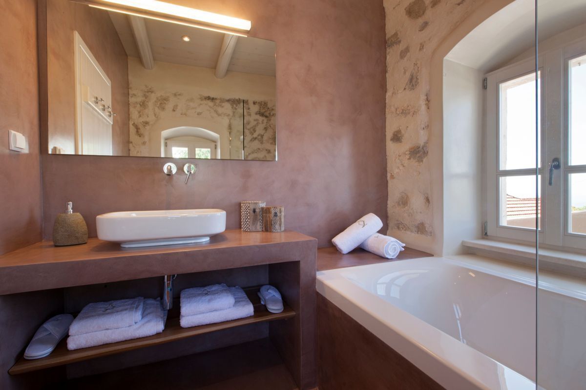A bathroom with a large mirror, a white sink, and a bathtub. There are towels and slippers on the counter.