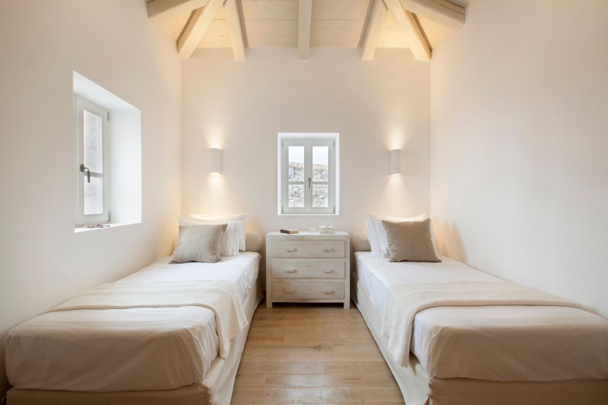 A bedroom with two single beds, a nightstand, a window, and wall-mounted lights.