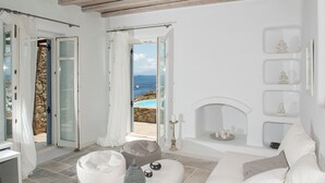 A white room with a stone wall, a fireplace, and a view of the sea.
